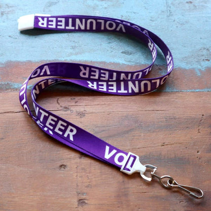 A 10 Pack - Volunteer Lanyard with Badge Set - Pre-Printed Volunteer Design - Dual Sided lies on a wooden surface, ready to hold a badge. Sold by Specialist ID.
