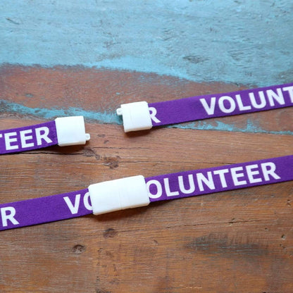 Three items from the 10 Pack - Volunteer Lanyard with Badge Set - Pre-Printed Volunteer Design - Dual Sided, marked with the word "VOLUNTEER" in white, are placed on a wooden surface, each resembling a badge of honor.