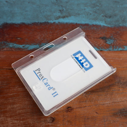 A Horizontal 70 - 90 Mil ProxCard II / Thick HID Proximity Card Holder (SPID-PROX-H) on a wooden surface contains a white ProxCard II by HID Corporation.