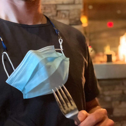 Person wearing an Adjustable Length Double Ended Lanyard - Handy & Convenient Event Badge Holder & Hanger with 2 Clips around their neck, holding a fork while seated indoors with a fireplace in the background.