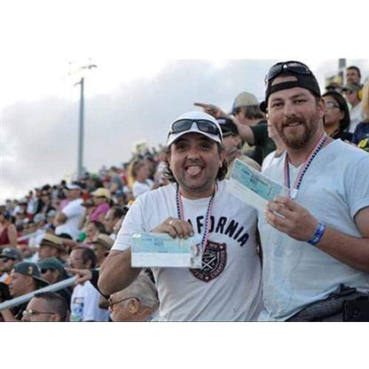 Two men standing and smiling in a crowded stadium, holding tickets. One man is wearing a white t-shirt with "California" on it, while the other has a black cap, blue long sleeve shirt, and an oversized Vertical Oversized 4X7 Vinyl ID Badge & Ticket Holder (XL47.5V) around his neck.