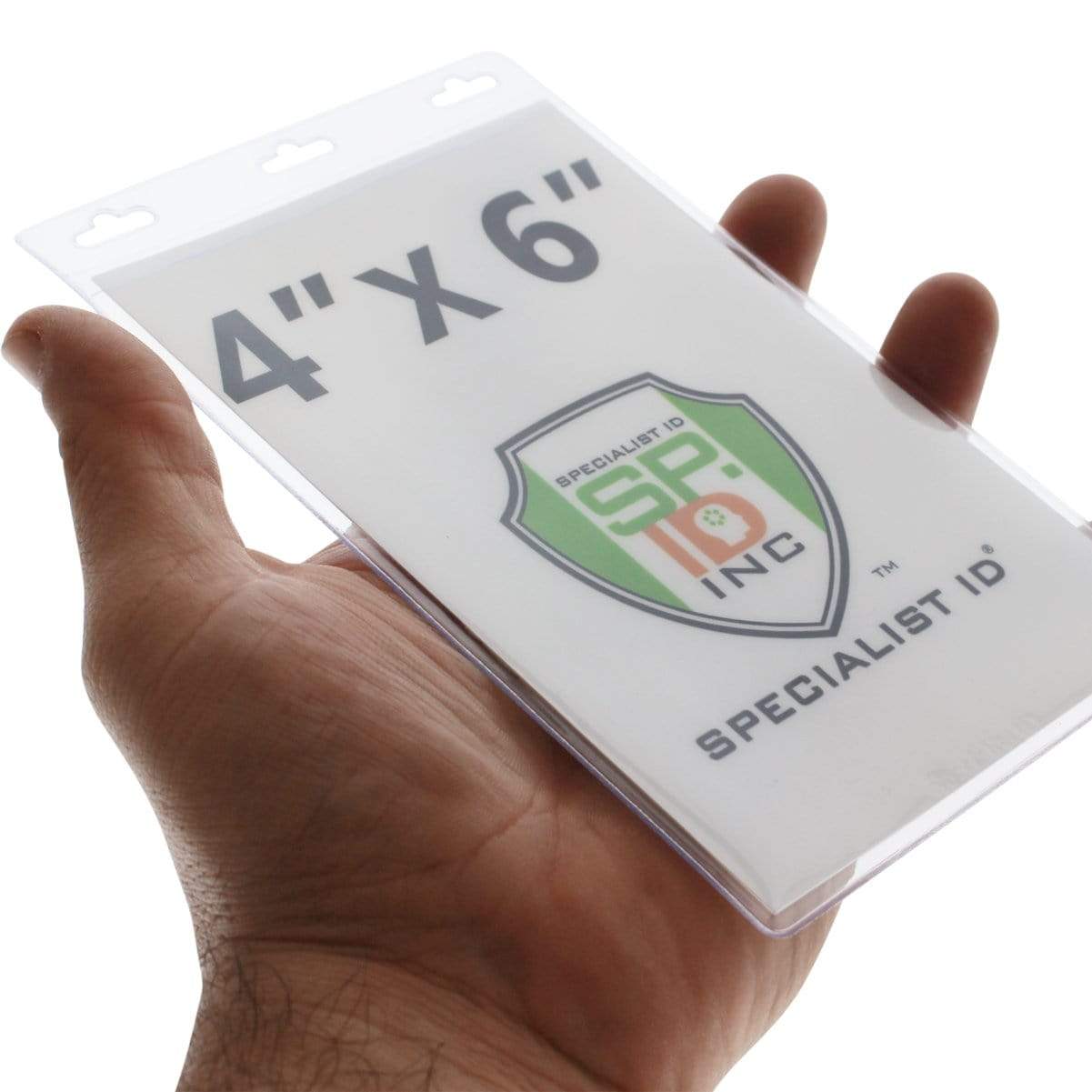 A hand holding a clear plastic holder with a paper insert displaying text "4"" x 6"" and a logo with "SP" on a shield. The text "SPECIALIST ID" is printed at the bottom of the insert, making it ideal for those needing special size credential holders or Vertical Oversized 4X6 Vinyl ID Badge Holder (XL46V).